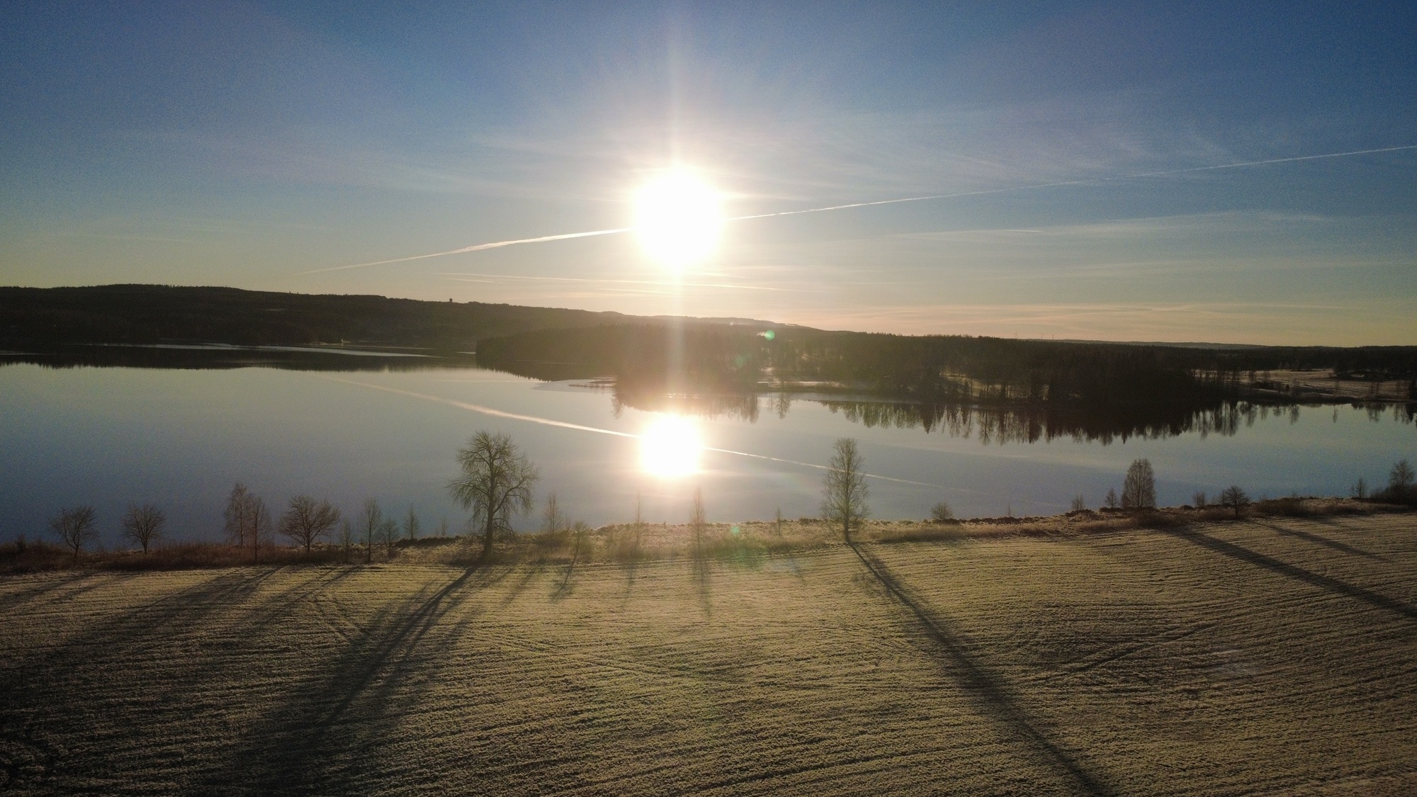 Sunrise over a calm Swedish lake with frosted fields and forest reflections